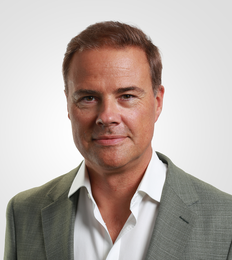 Portrait of a man with brown hair and glasses on a flat gray background.