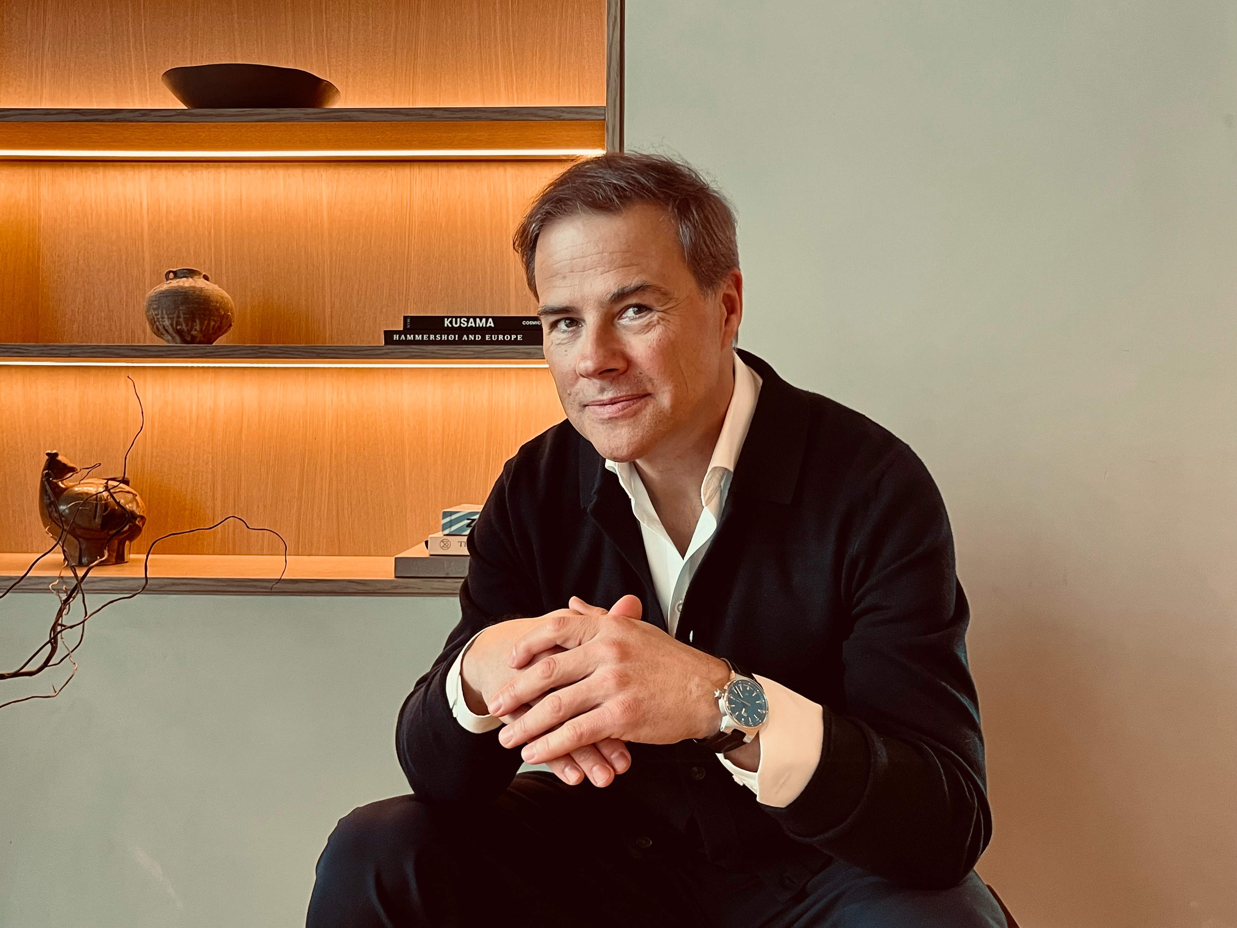 Portrait of a man with brown hair and glasses on a flat gray background.